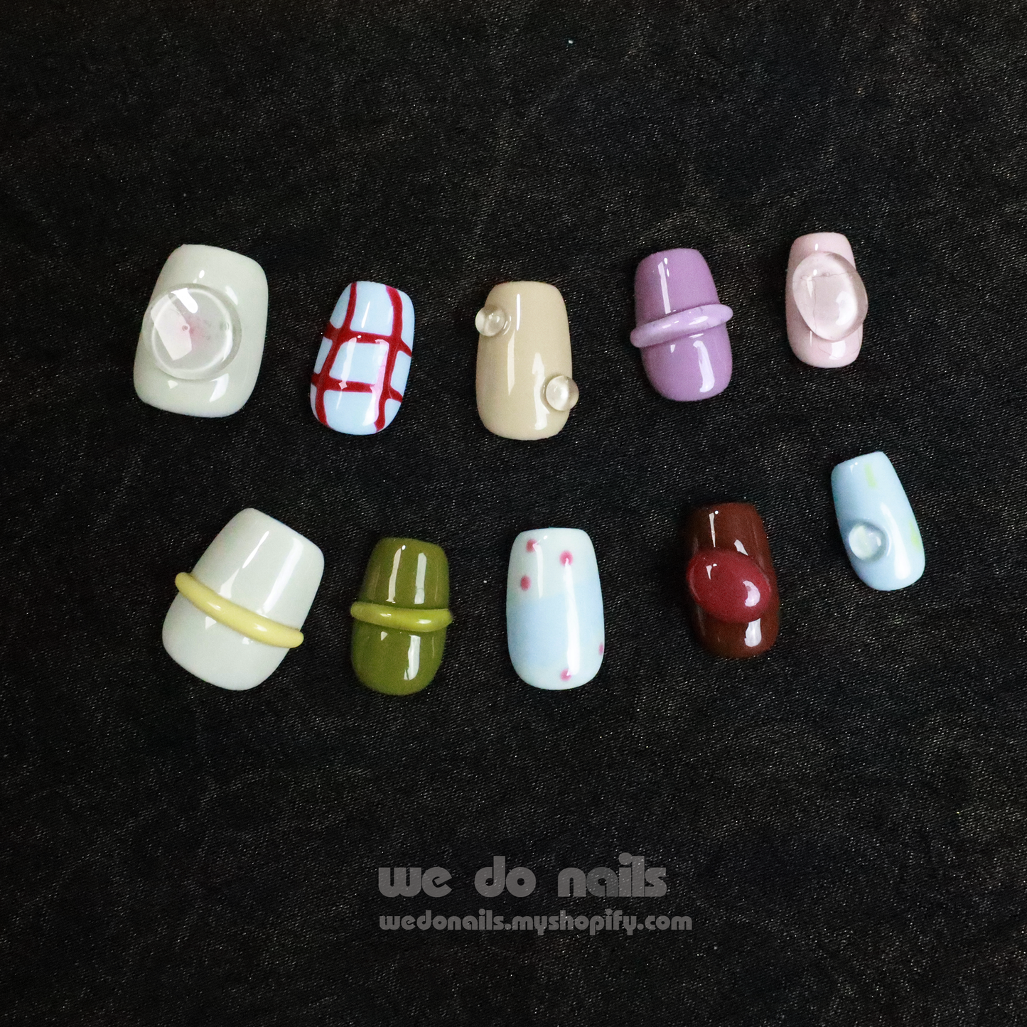 Close-up of colorful hands against a dark background, featuring We Do Nails Cute Abstract Art Press-On Nails with vibrant patterns like stripes and polka dots. Some nails have 3D finishes and embellishments, complemented by several rings on the persons fingers.