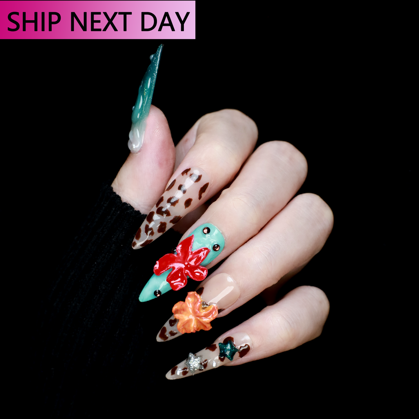 A hand with long, decorated Wild Coastal Charm Press-On Nails by We Do Nails showcases a mint green nail with a red bow, cheetah and animal prints, and 3D floral accents. A Ship Next Day label is in the top left corner against a sleek black background.