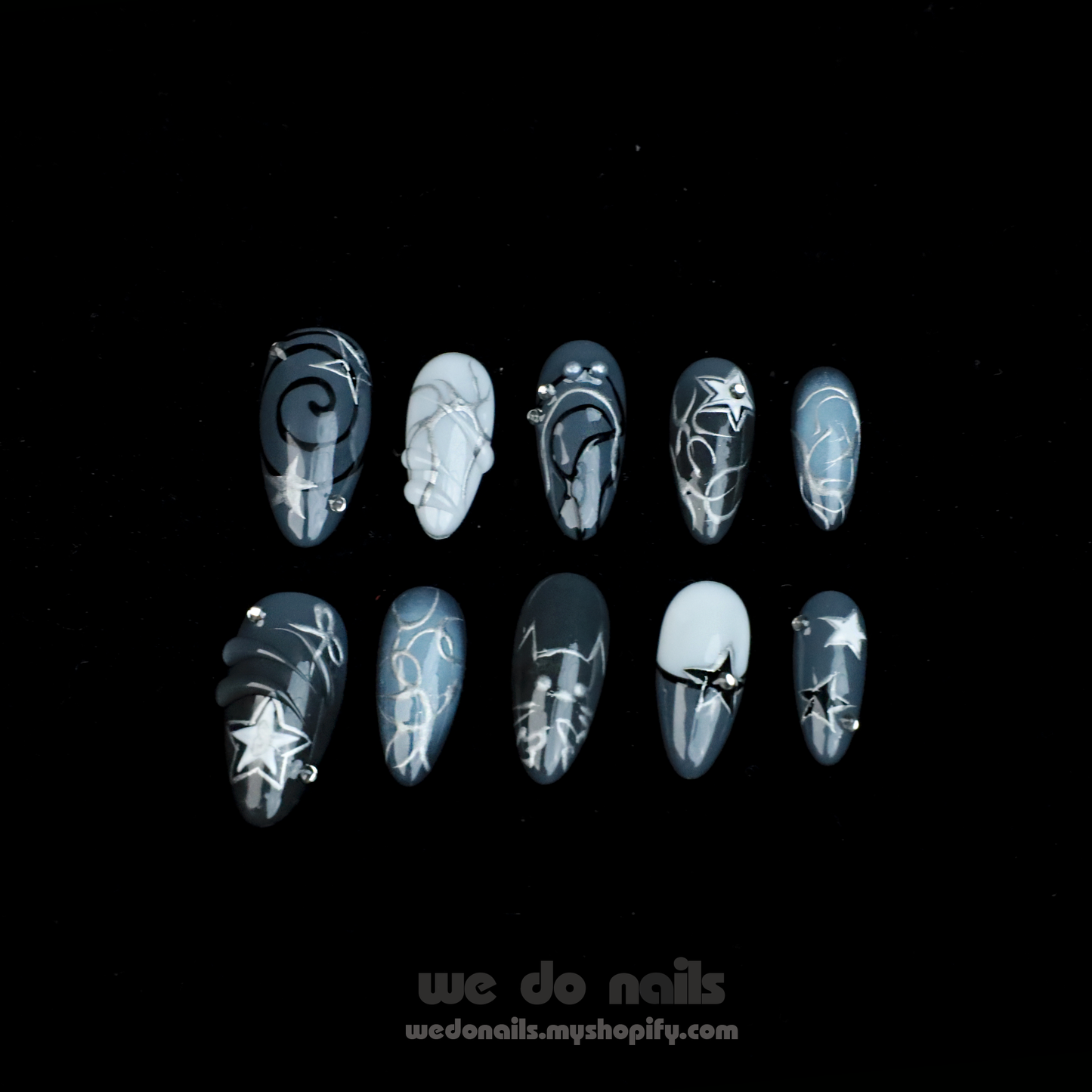 A person holds a white mug with both hands, showcasing long, pointed nails from We Do Nails Midnight Custom Press-On Nails. Star and galaxy designs exude cosmic elegance against a dark background, enhancing the vibrant celestial wonder of the nail art.