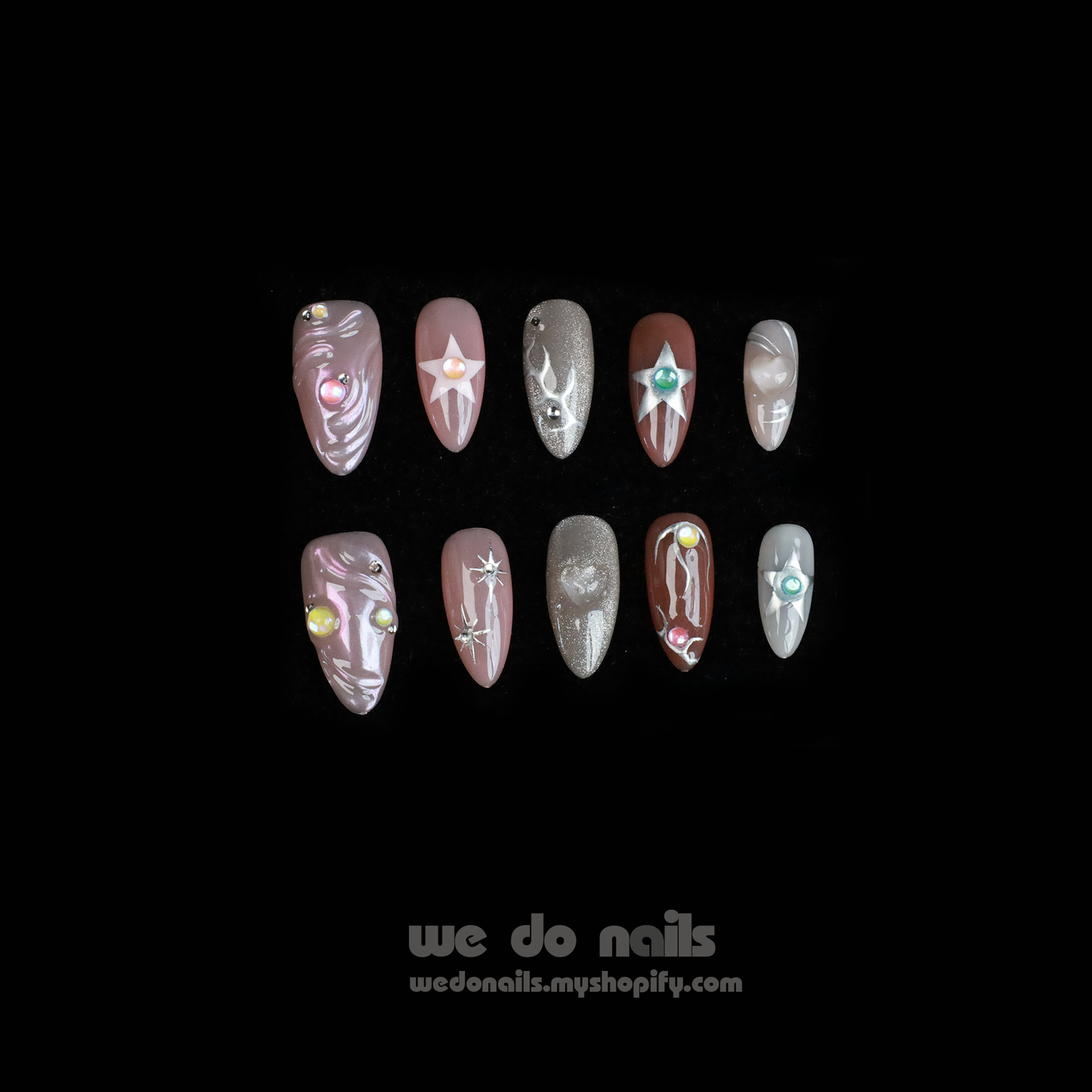 Two hands with long, decorated nails hold a white ceramic mug. Featuring Shiny Star Press-On Nails by We Do Nails, the celestial-inspired manicure showcases flowers, stars, and glitter. Against a dark background, We Do Nails and a URL add allure to this luminous display.