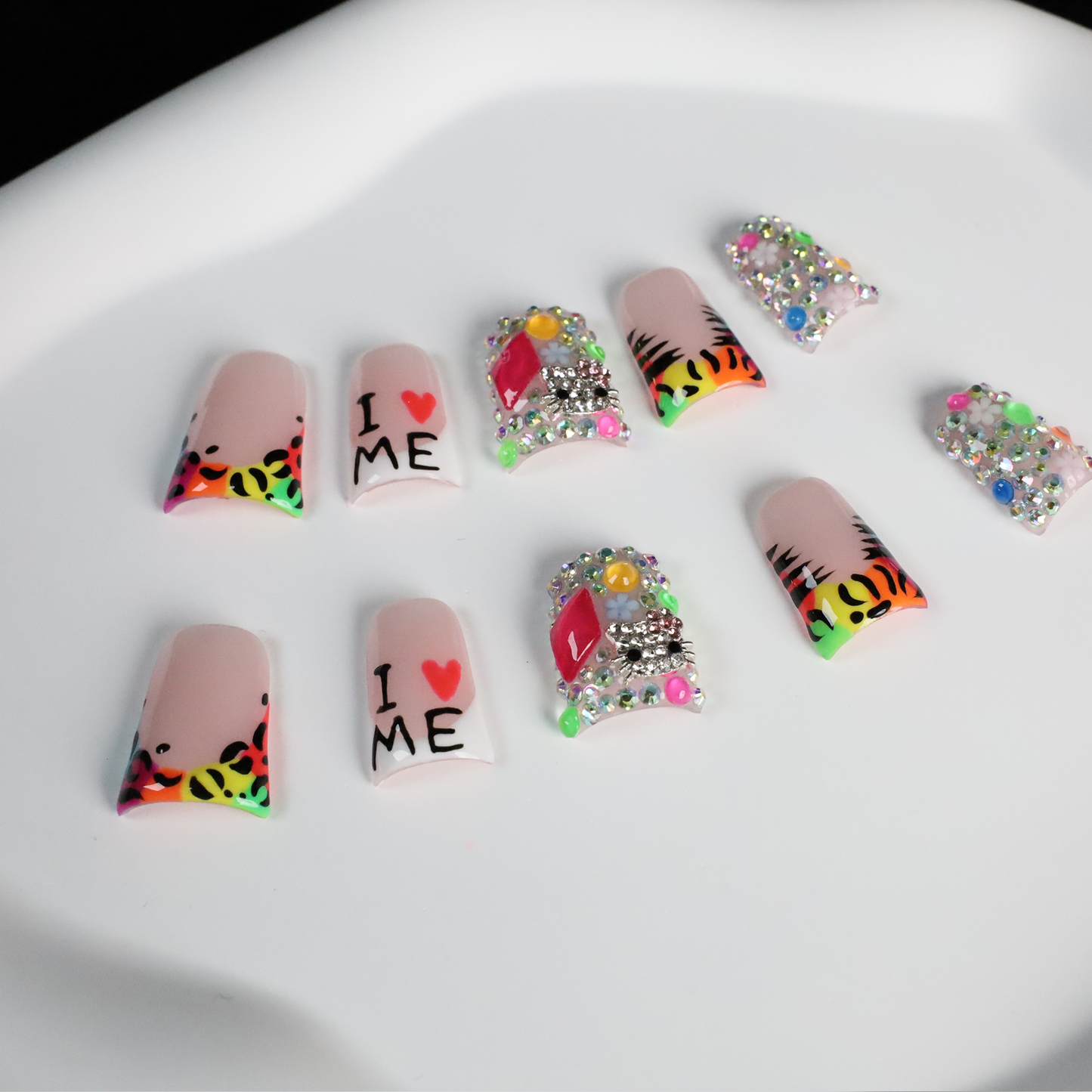 A pair of hands showcases long, decorated nails with Y2K-inspired art, including hearts and lettering. A pink banner reads SHIP NEXT DAY. The black backdrop highlights the vibrant leopard and tiger print accents on these striking Neon Safari Short Duck Press-On Nails by We Do Nails.