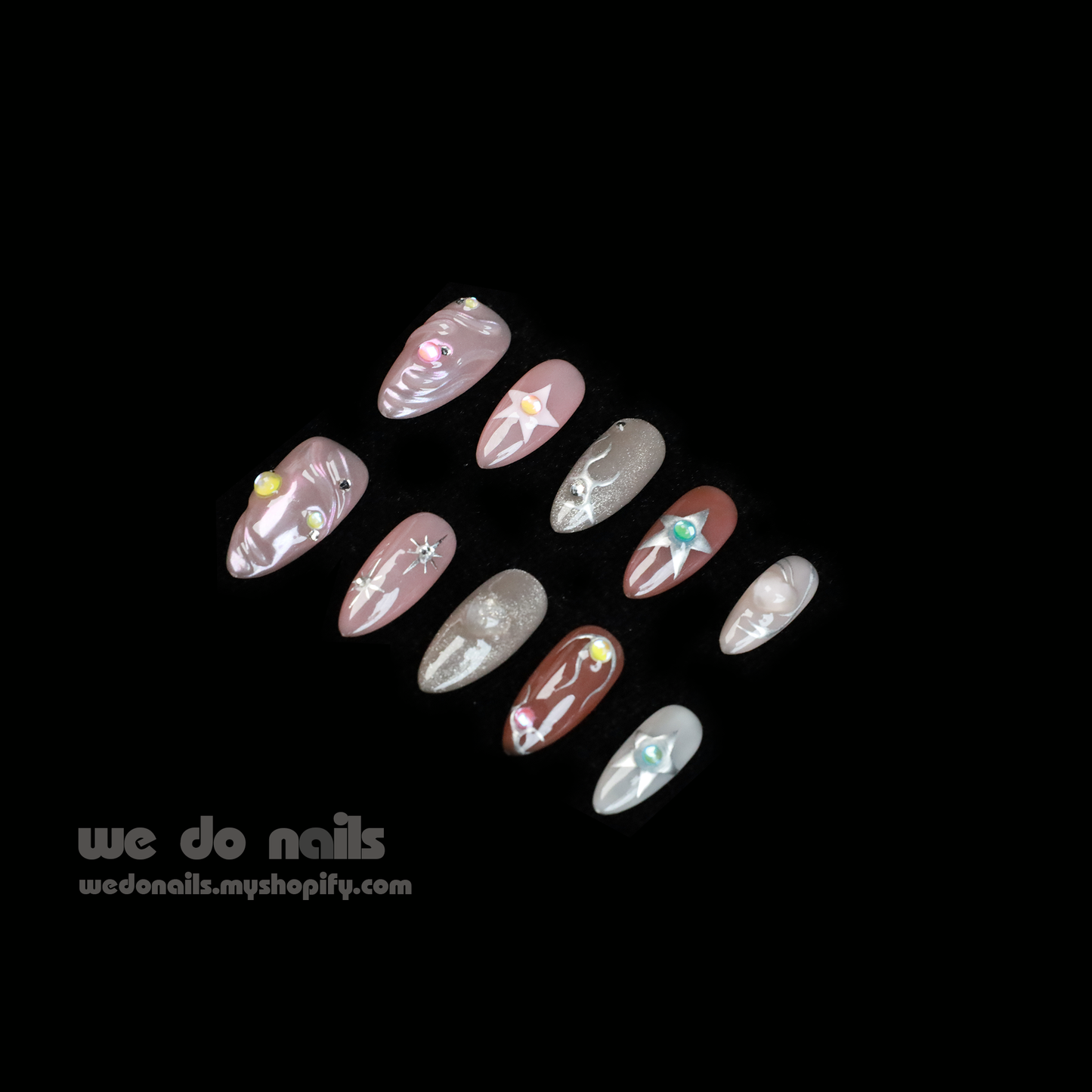 Two hands with long, decorated nails hold a white ceramic mug. Featuring Shiny Star Press-On Nails by We Do Nails, the celestial-inspired manicure showcases flowers, stars, and glitter. Against a dark background, We Do Nails and a URL add allure to this luminous display.