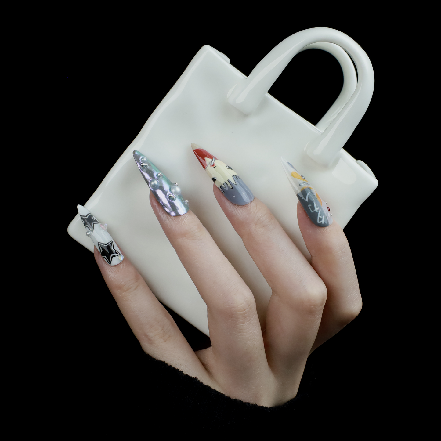 A hand with long, pointed Japanese-Inspired Artistic Press-On Nails by We Do Nails showcases camo patterns in green, red, and gray. Combining kawaii aesthetic and artistic motifs that suggest anime nail art, the hand is partially covered by a black sleeve.