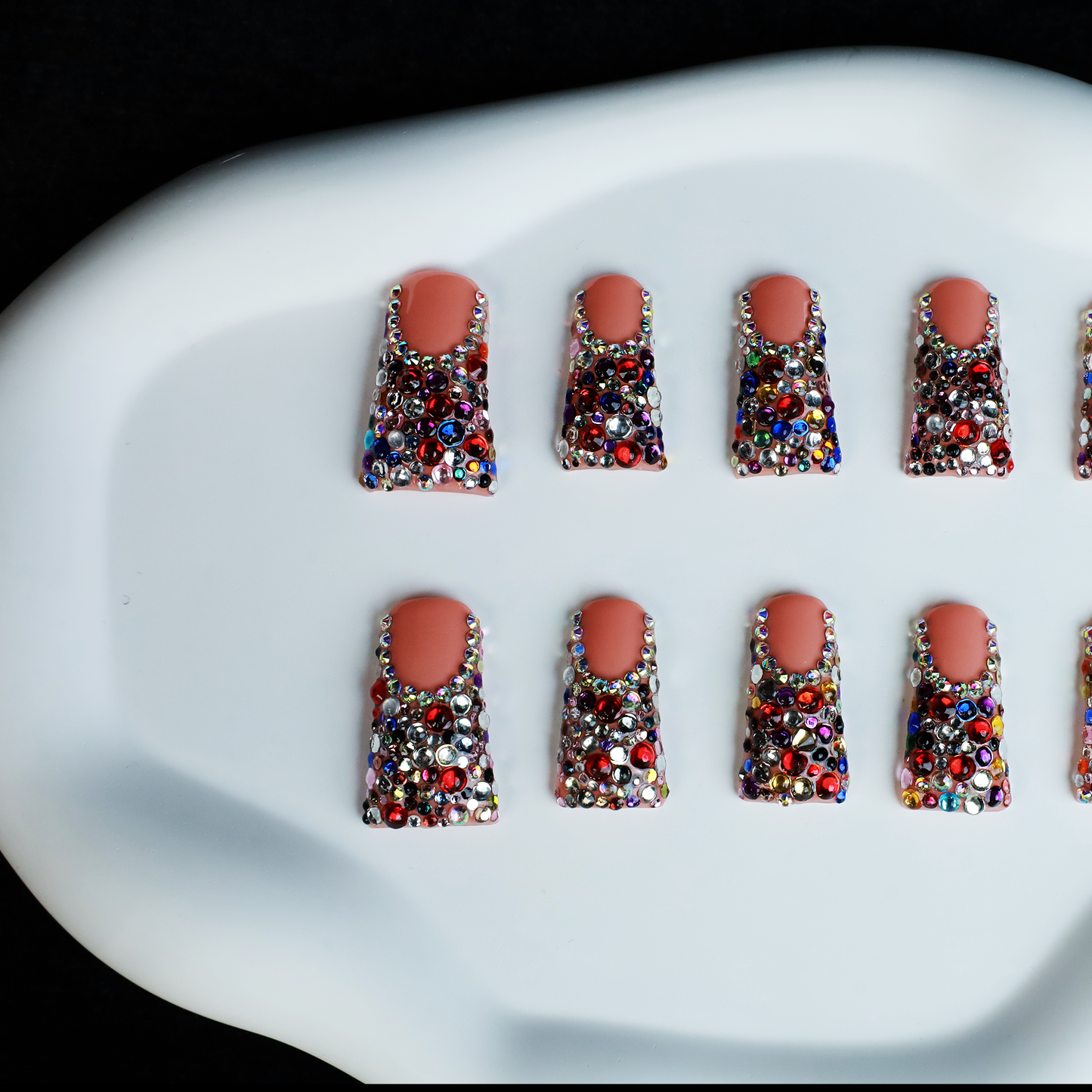 A hand flaunts Dazzling Long Duck Press-On Nails from We Do Nails, featuring a nude pink base with multicolored rhinestones against a black background. The SHIP NEXT DAY label is clearly visible in the top left corner.