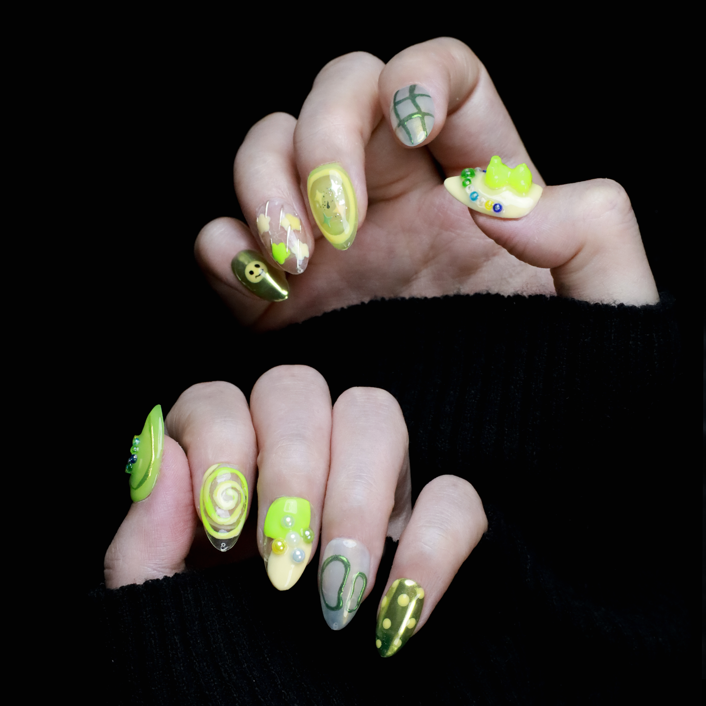 A hand holding a black mug flaunts vibrant We Do Nails Neon Slime Fantasy Press-On Nails, featuring abstract lime green, yellow, and black patterns. Spirals, dots with bead accents, and 3D smiley faces create playful art against the dark backdrop.