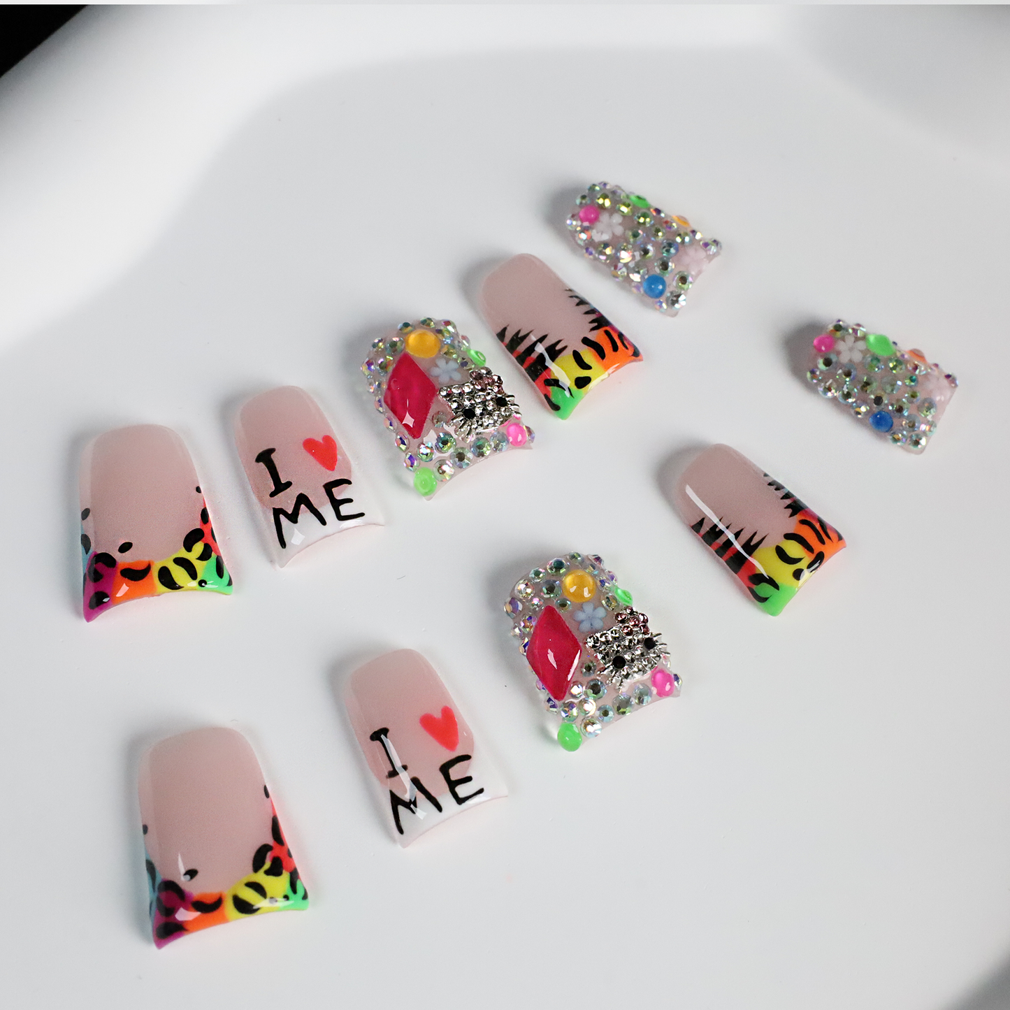 A pair of hands showcases long, decorated nails with Y2K-inspired art, including hearts and lettering. A pink banner reads SHIP NEXT DAY. The black backdrop highlights the vibrant leopard and tiger print accents on these striking Neon Safari Short Duck Press-On Nails by We Do Nails.