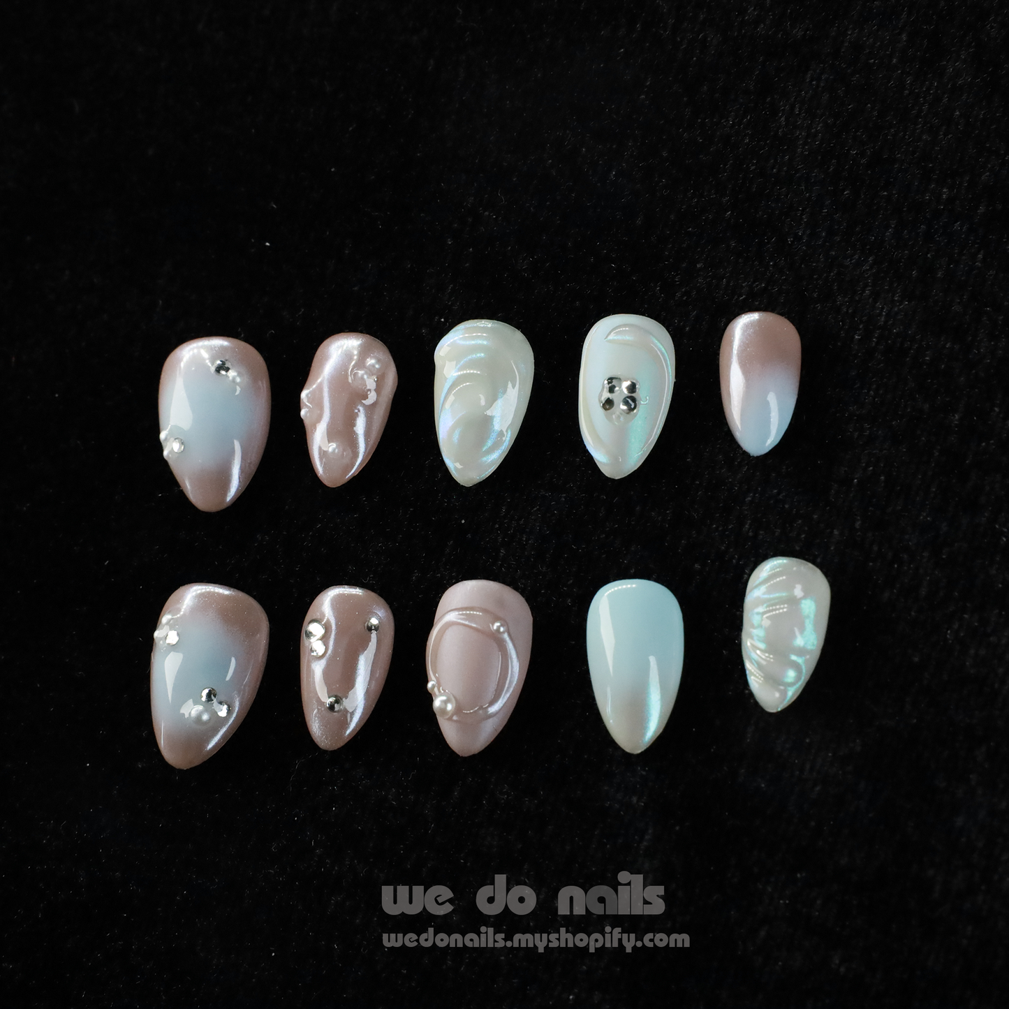Close-up of hands with Pearl Dreams Press-On Nails by We Do Nails, showcasing manicured nails in small patterns and neutral colors. Subtle pearlescent hues add elegance. Fingers are gently intertwined, wearing a black long-sleeve sweater. We Do Nails text visible on the left.