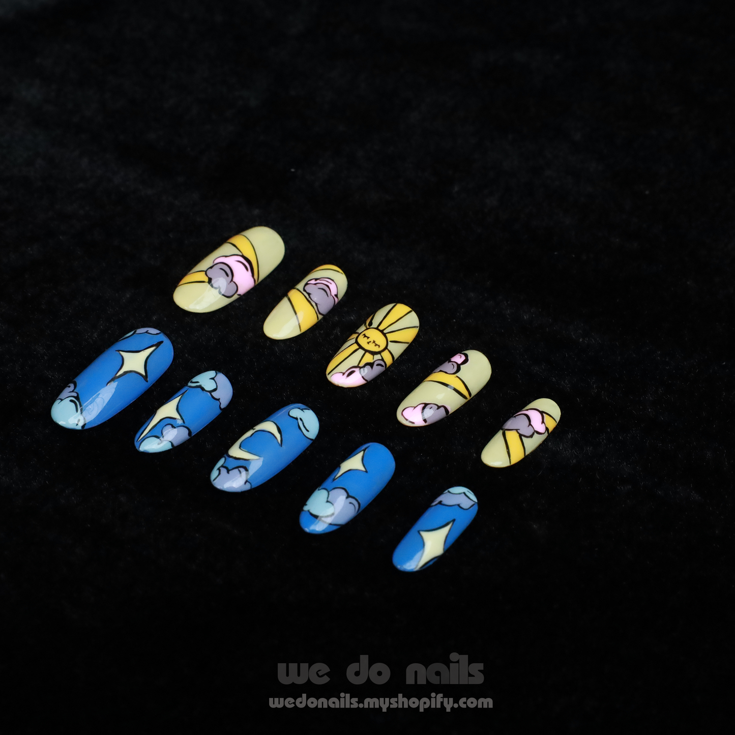 Close-up of hands showcasing artistic nail designs from We Do Nails. One set, Sunrise, features yellow nails with flowers and the other, Moonlight, displays blue nails with cloud patterns. The person is in a black sweater with a logo visible at the bottom left.