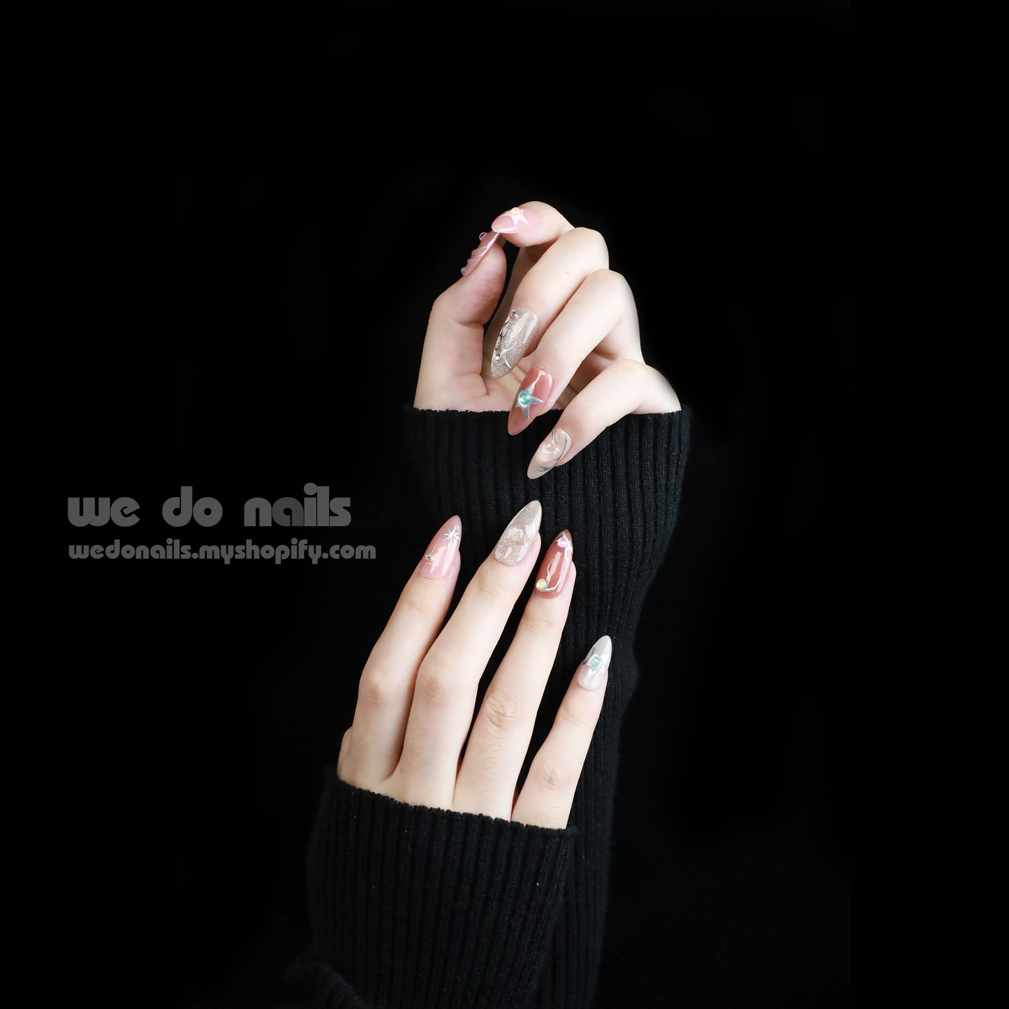 Two hands with long, decorated nails hold a white ceramic mug. Featuring Shiny Star Press-On Nails by We Do Nails, the celestial-inspired manicure showcases flowers, stars, and glitter. Against a dark background, We Do Nails and a URL add allure to this luminous display.