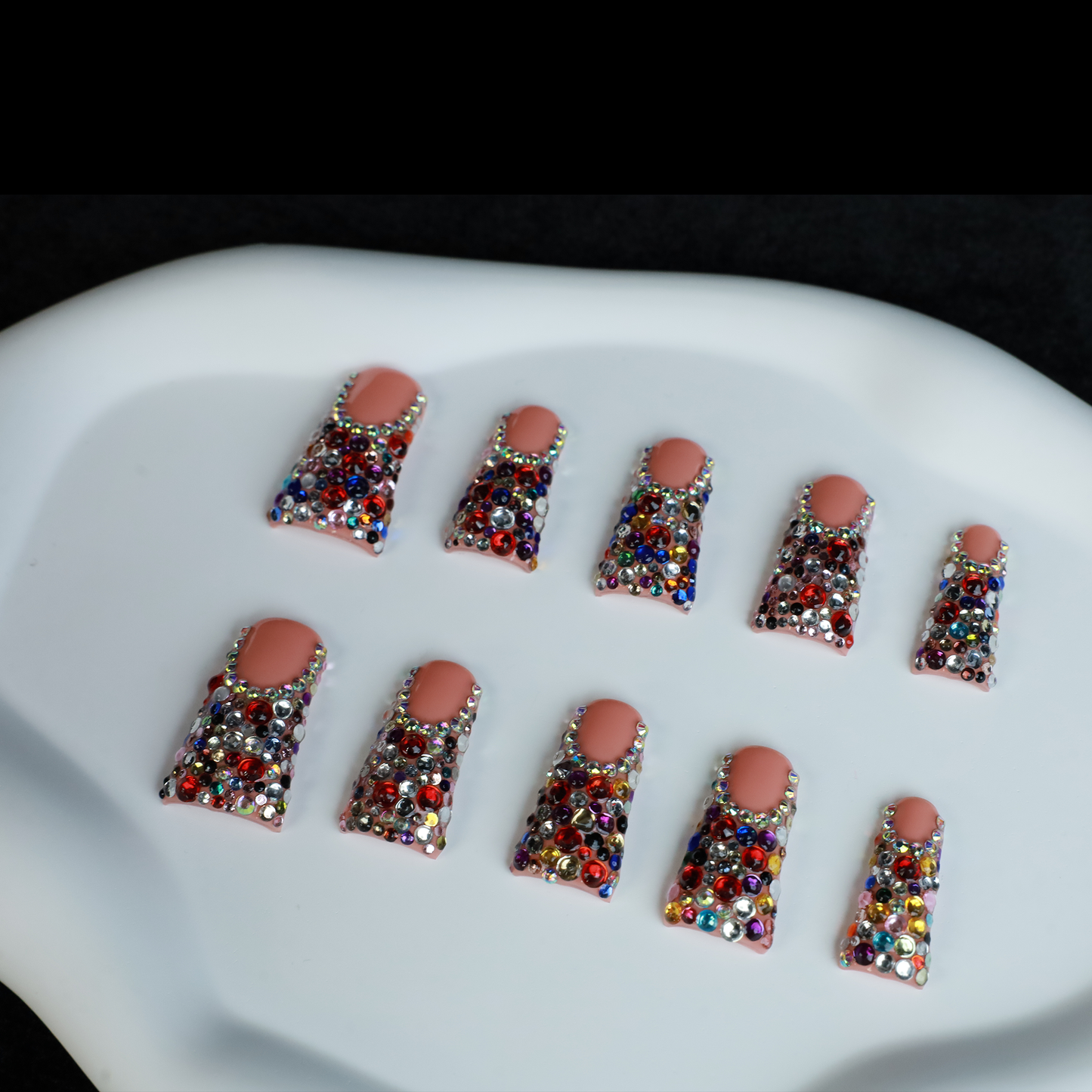 A hand flaunts Dazzling Long Duck Press-On Nails from We Do Nails, featuring a nude pink base with multicolored rhinestones against a black background. The SHIP NEXT DAY label is clearly visible in the top left corner.