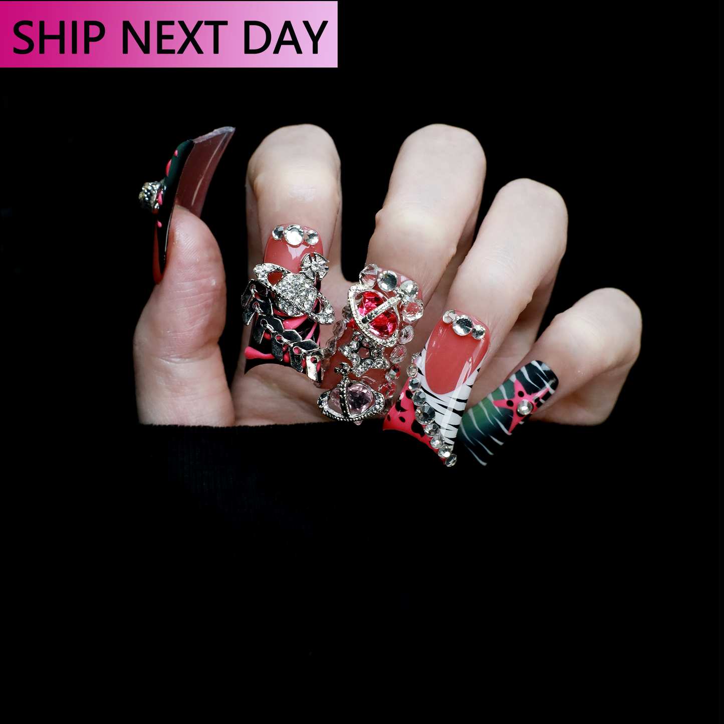 A hand displays Glam Jungle Luxe 3D Long Duck Press-On Nails by We Do Nails, featuring ornate black and red designs with rhinestone gemstones and skulls. The words SHIP NEXT DAY appear in the top-left corner, highlighting their gothic style against a dark background.