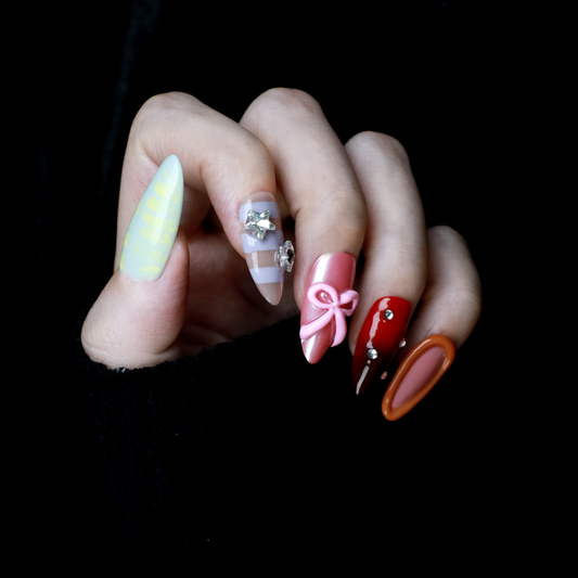A hand with We Do Nails Candyland Dream Press-On Nails displays playful designs. Features include pastel yellow plaid, clear nails with bows and rhinestones, pink nails with a bow, shiny red with rhinestones, and glossy rust-orange—all set against a dark backdrop.