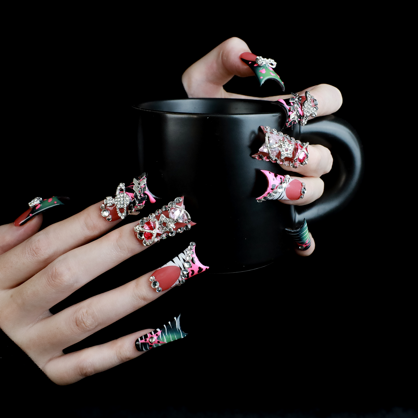 A hand displays Glam Jungle Luxe 3D Long Duck Press-On Nails by We Do Nails, featuring ornate black and red designs with rhinestone gemstones and skulls. The words SHIP NEXT DAY appear in the top-left corner, highlighting their gothic style against a dark background.