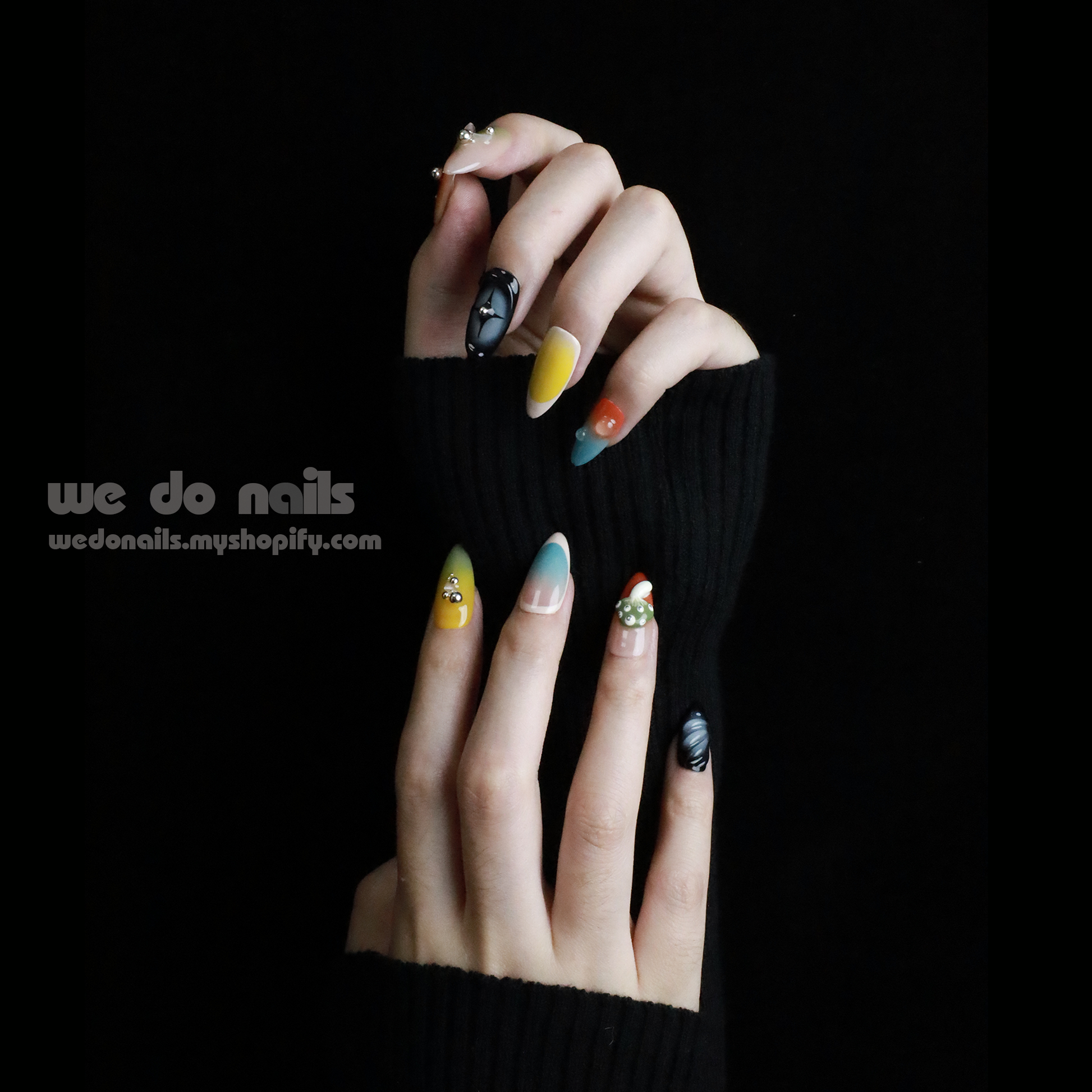 Two hands with unique, long nails showcase vibrant designs, including stripes and rhinestones, shimmering against a black backdrop. A black sleeve covers part of one hand. We Do Nails Nettle Forest Press-On Nails feature an exquisite 3D design that elevates manicures.