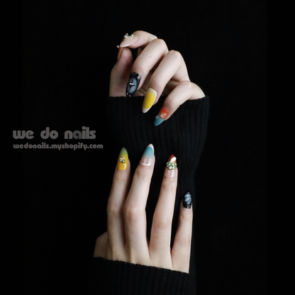 Two hands with unique, long nails showcase vibrant designs, including stripes and rhinestones, shimmering against a black backdrop. A black sleeve covers part of one hand. We Do Nails Nettle Forest Press-On Nails feature an exquisite 3D design that elevates manicures.