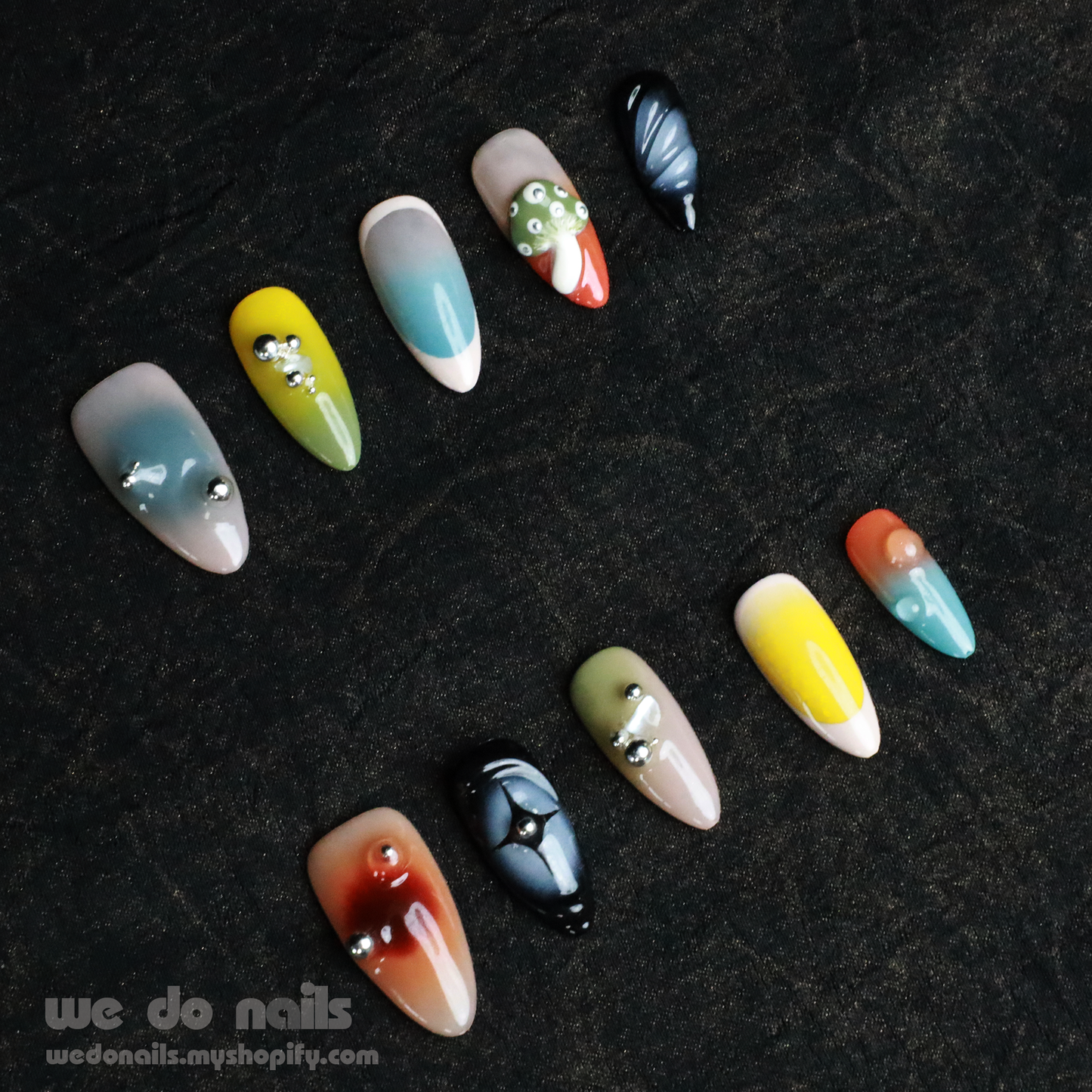 Two hands with unique, long nails showcase vibrant designs, including stripes and rhinestones, shimmering against a black backdrop. A black sleeve covers part of one hand. We Do Nails Nettle Forest Press-On Nails feature an exquisite 3D design that elevates manicures.