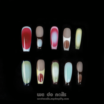 A pair of hands with long, artistic Ms.Circles Press-On Nails by We Do Nails stand out against a black background. The vibrant nails have bold patterns in green, pink, and nude hues. Partially emerging from black sweater sleeves, they create a striking contrast.