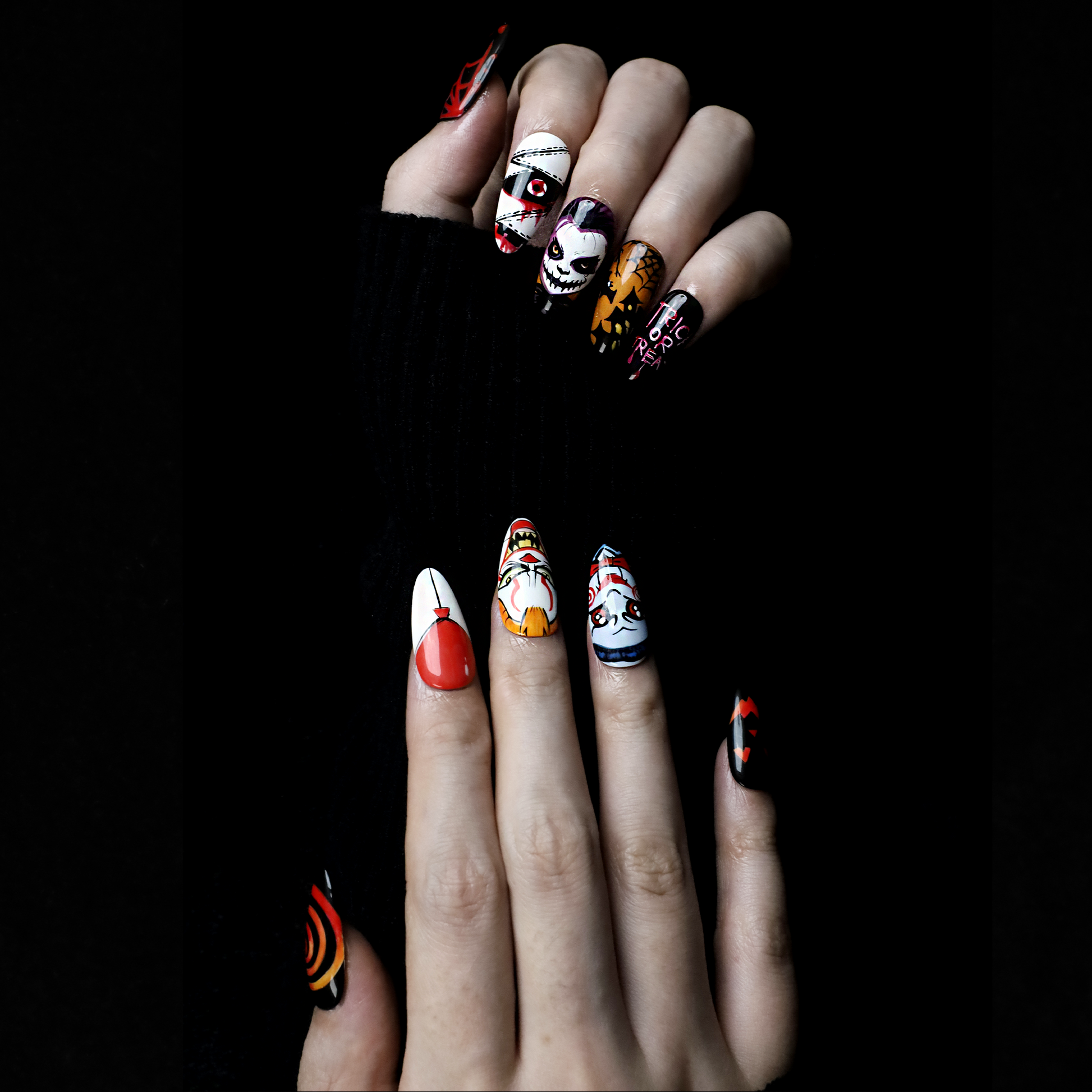 A close-up of two hands shows off the eerie Spooky Nightmares Halloween Press-On Nails by We Do Nails, featuring hand-painted designs like clowns, a pumpkin, and abstract art on a black background while holding a large white mug.