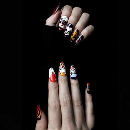 A close-up of two hands shows off the eerie Spooky Nightmares Halloween Press-On Nails by We Do Nails, featuring hand-painted designs like clowns, a pumpkin, and abstract art on a black background while holding a large white mug.