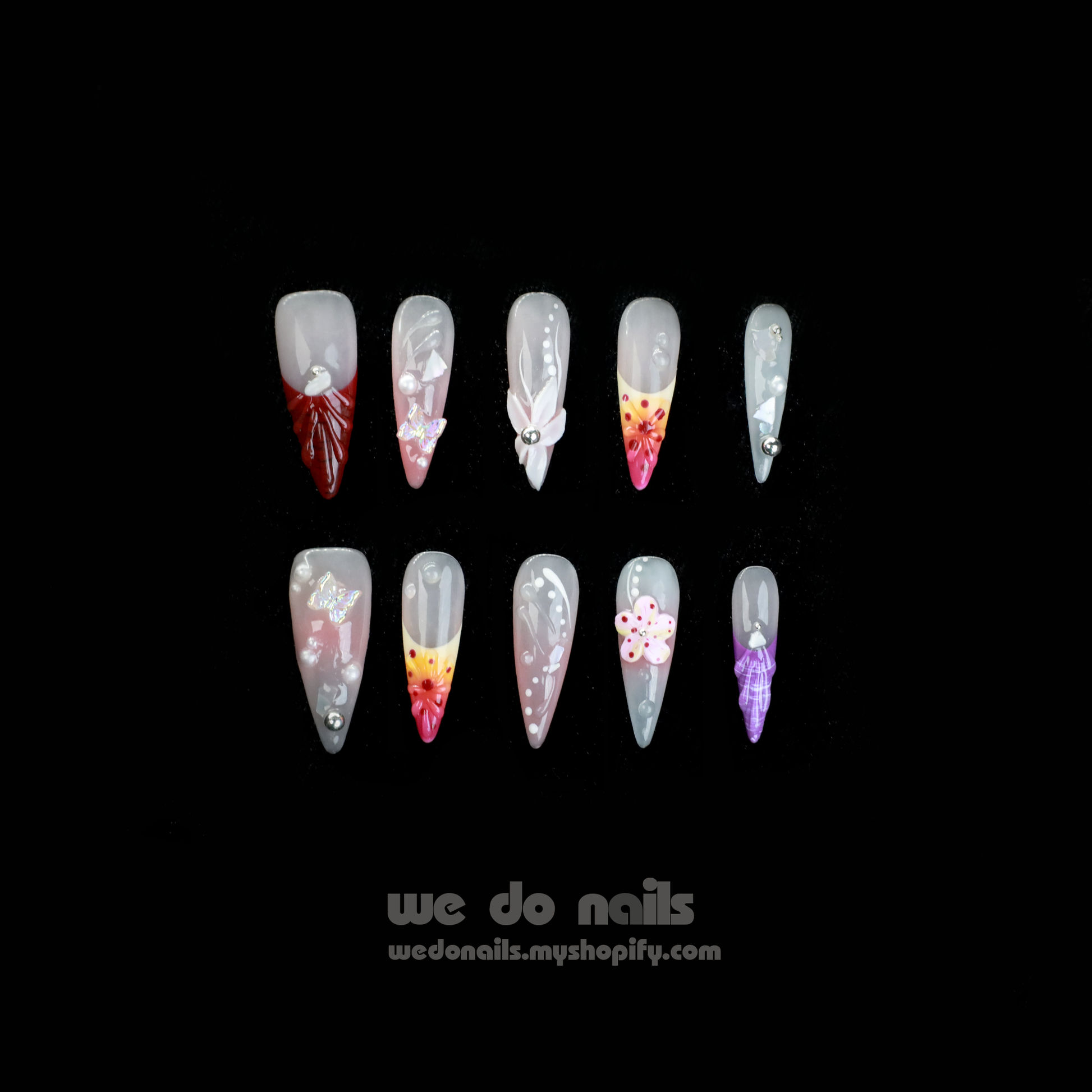 A hand flaunting Floral Fantasy Press-On Nails, accented with 3D flowers and rhinestones, grasps a large black mug. Against a dark backdrop, the foreground displays the text We Do Nails with their nail shop URL.