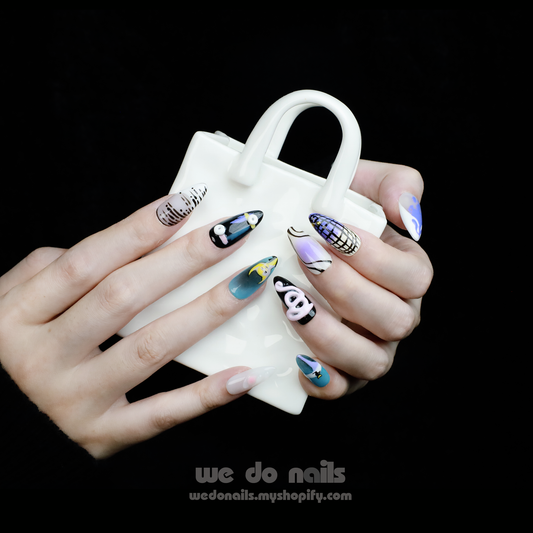 Someone with long, artistic Mystic Dream Press-On Nails by We Do Nails holds a small white handbag. The nails, part of the collection, showcase abstract designs, patterns, faces, and vibrant colors on a black background.