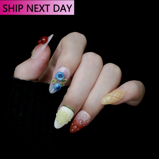 The Tutti-Fruit Charm Press-On Nails by We Do Nails feature long, sculpted designs with 3D fruits like cherries and blueberries, plus a flower and fruit patterns on a black background. A pink and black label at the top says SHIP NEXT DAY.