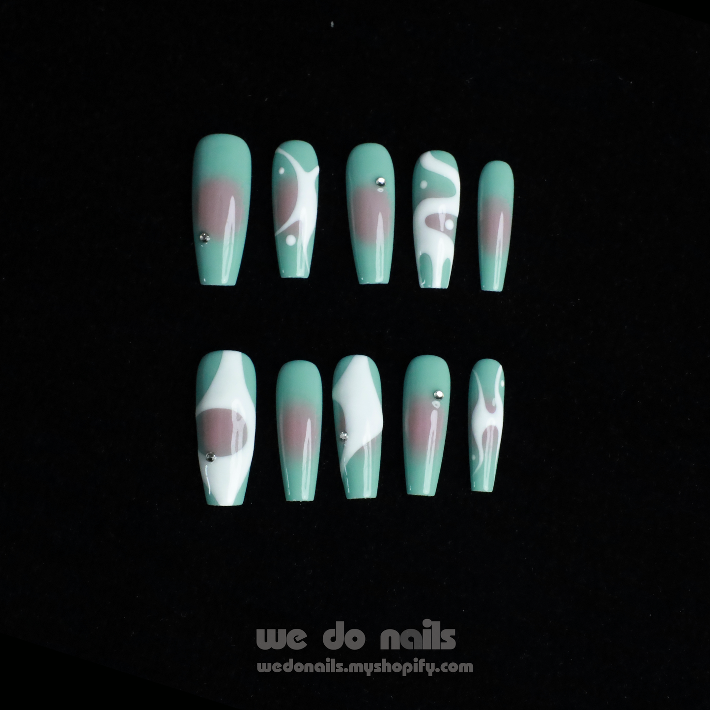 Hands with long, angular green nails pose gracefully against a black background, showcasing a modern and stylish design. The glossy finish and rings add flair, elegantly highlighting the allure of Spilled Milk Press-On Nails by We Do Nails.