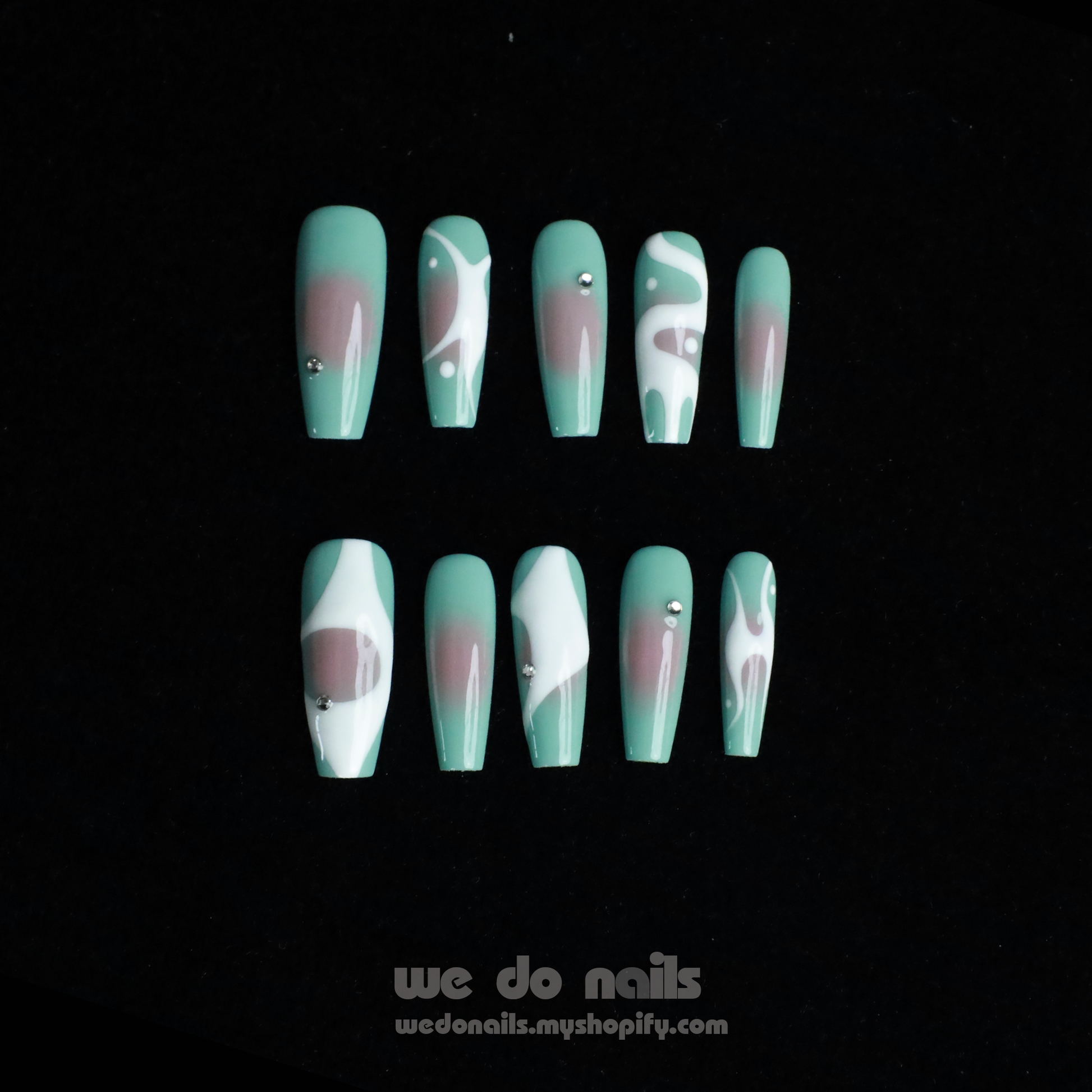 Hands with long, angular green nails pose gracefully against a black background, showcasing a modern and stylish design. The glossy finish and rings add flair, elegantly highlighting the allure of Spilled Milk Press-On Nails by We Do Nails.