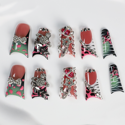A hand displays Glam Jungle Luxe 3D Long Duck Press-On Nails by We Do Nails, featuring ornate black and red designs with rhinestone gemstones and skulls. The words SHIP NEXT DAY appear in the top-left corner, highlighting their gothic style against a dark background.