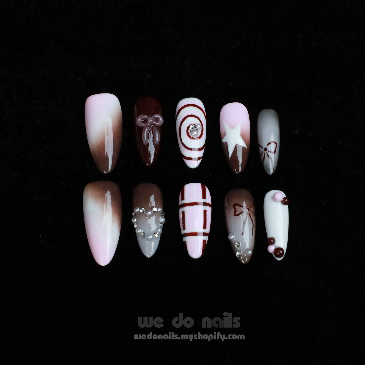 A hand with enchanting nails holds a small white handbag. The Charming Cocoa Delight Press-On Nails from We Do Nails showcase intricate patterns, featuring stripes and dotted embellishments in white, brown, and red shades, all set against a black background that enhances their allure.