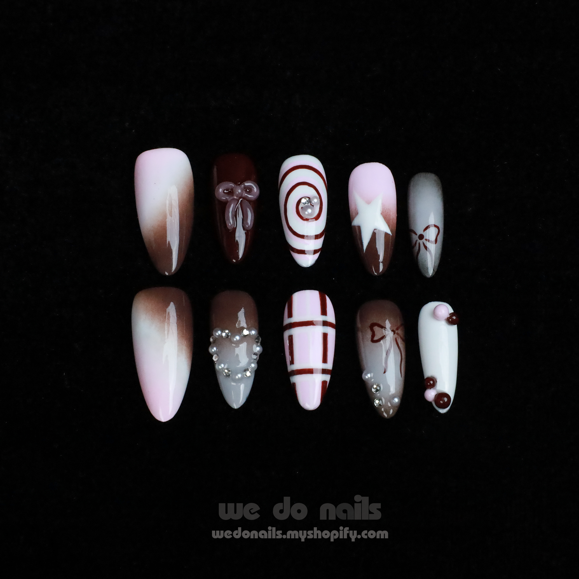 A hand with enchanting nails holds a small white handbag. The Charming Cocoa Delight Press-On Nails from We Do Nails showcase intricate patterns, featuring stripes and dotted embellishments in white, brown, and red shades, all set against a black background that enhances their allure.