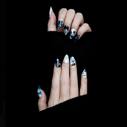 Hands adorned with We Do Nails Blue & White Porcelain Inspired Nails, showcasing long, almond-shaped designs with intricate traditional floral and abstract patterns. The nails stand out against black sleeves and a black background, reflecting the elegance of Chinese porcelain.