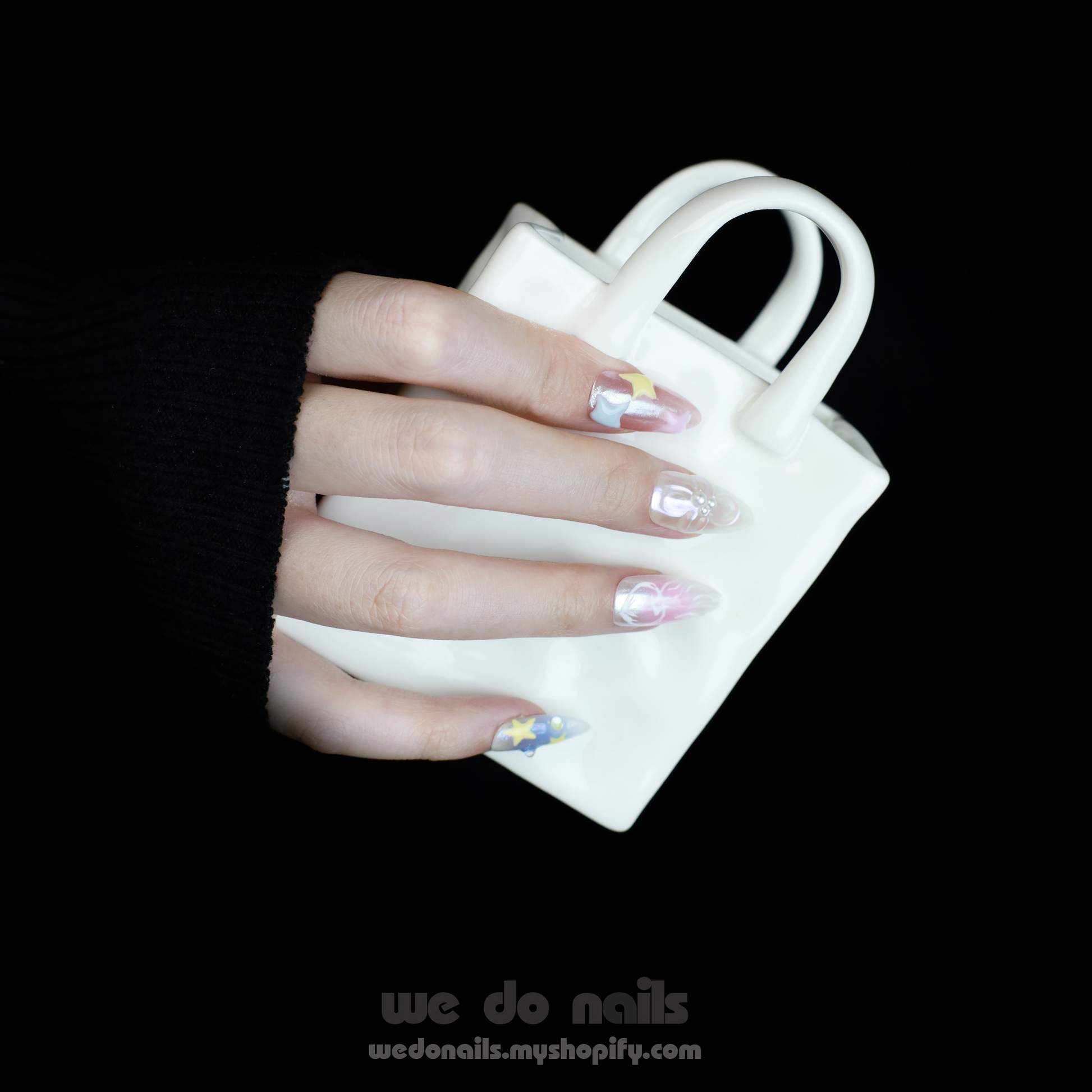 A hand with long, intricately designed Ocean-Themed Press-On Nails by We Do Nails holds a small white ceramic purse. The nails feature pastel floral and star marine motifs. A pink SHIP NEXT DAY banner appears in the top left corner.