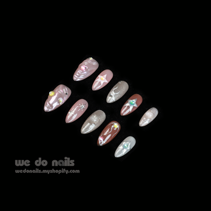 Two hands with long, decorated nails hold a white ceramic mug. Featuring Shiny Star Press-On Nails by We Do Nails, the celestial-inspired manicure showcases flowers, stars, and glitter. Against a dark background, We Do Nails and a URL add allure to this luminous display.