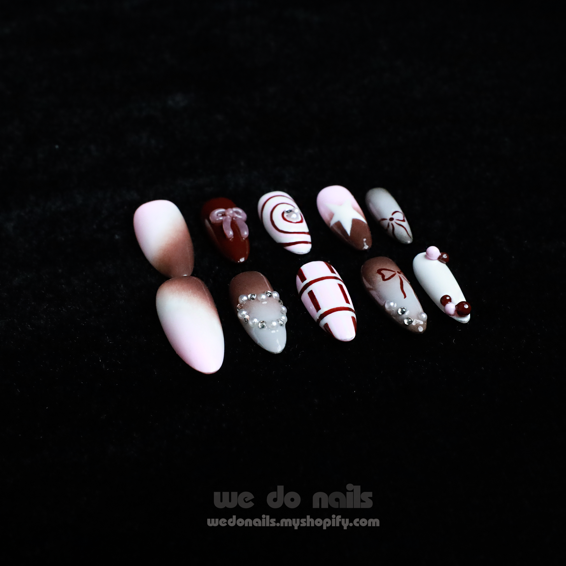 A hand with enchanting nails holds a small white handbag. The Charming Cocoa Delight Press-On Nails from We Do Nails showcase intricate patterns, featuring stripes and dotted embellishments in white, brown, and red shades, all set against a black background that enhances their allure.