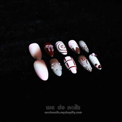 A hand with enchanting nails holds a small white handbag. The Charming Cocoa Delight Press-On Nails from We Do Nails showcase intricate patterns, featuring stripes and dotted embellishments in white, brown, and red shades, all set against a black background that enhances their allure.