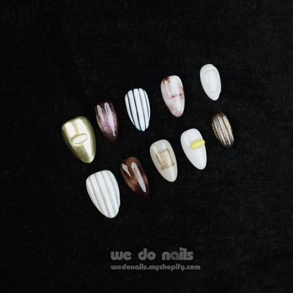 A hand with Elegant Press-On Nails holding a large white mug displays glittery stripes, marbling, and metallic textures with hints of gold. The black background has text: We Do Nails followed by the URL wedonails.myshopify.com.