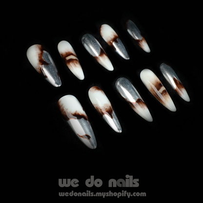 A pair of hands showcases Sizzling Marble Press-On Nails with a black and white marbled design, paired with a black long-sleeved sweater. Text includes We Do Nails and a URL. Stylish nails that redefine elegance!.