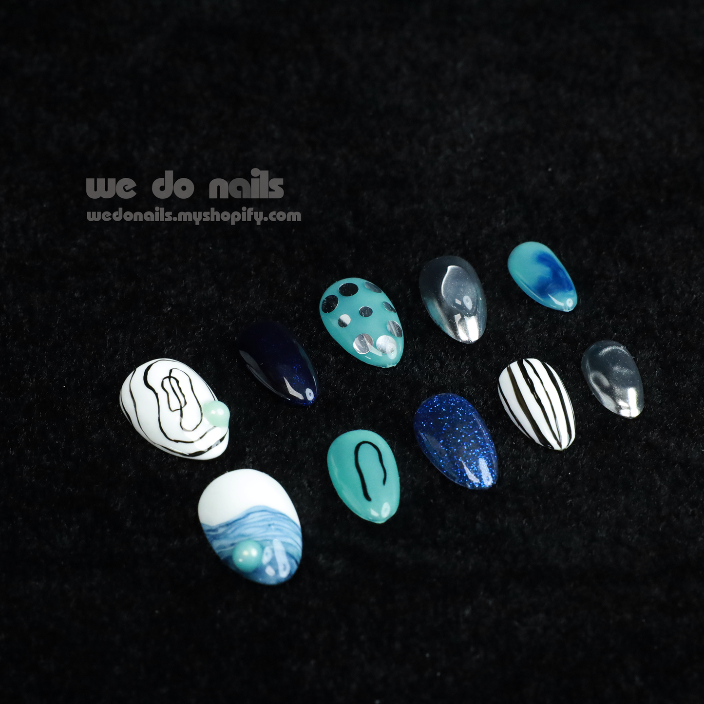 A person in a black sweater displays manicured fingernails with enchanting designs like polka dots, stripes, and abstract patterns. The metallic finishes shine in blue ombre and green hues, featuring Midnight Mystique Press-On Nails by We Do Nails. The text reads we do nails next to a website URL.