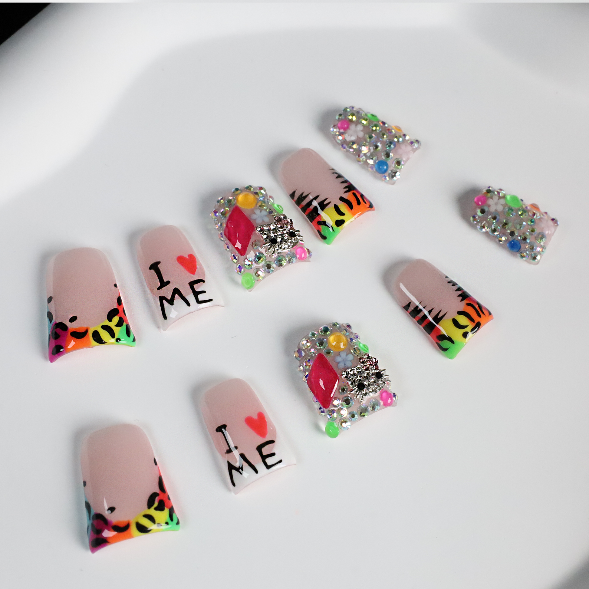 A pair of hands showcases long, decorated nails with Y2K-inspired art, including hearts and lettering. A pink banner reads SHIP NEXT DAY. The black backdrop highlights the vibrant leopard and tiger print accents on these striking Neon Safari Short Duck Press-On Nails by We Do Nails.