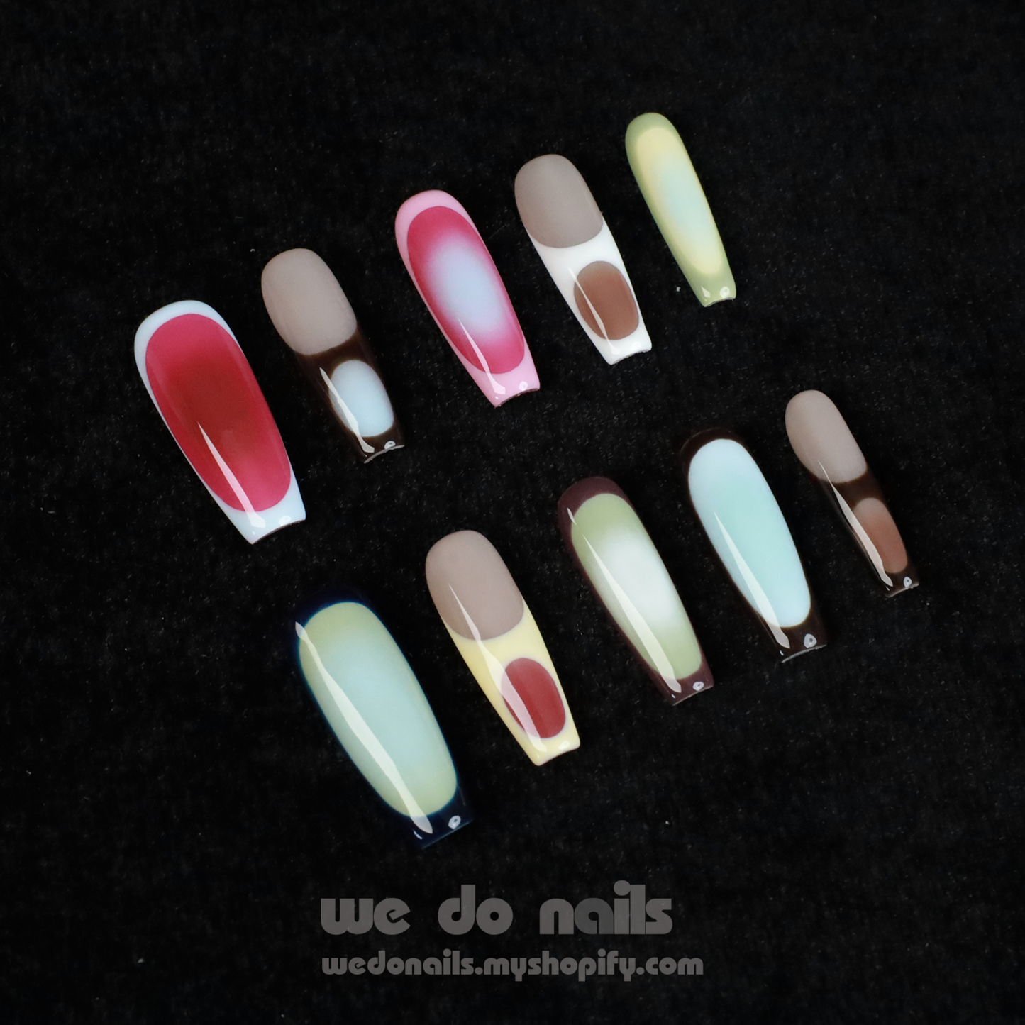 A pair of hands with long, artistic Ms.Circles Press-On Nails by We Do Nails stand out against a black background. The vibrant nails have bold patterns in green, pink, and nude hues. Partially emerging from black sweater sleeves, they create a striking contrast.