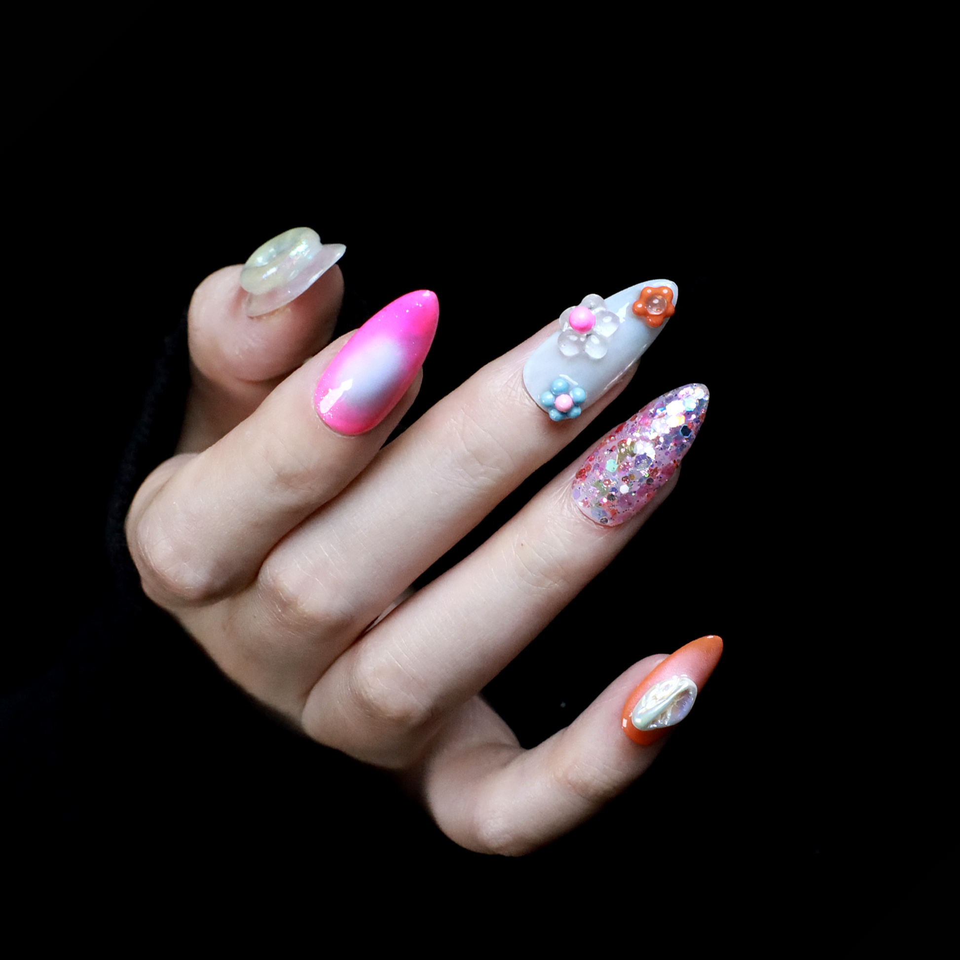 A hand features the Summer Island Press-On Nails by We Do Nails: glossy pearl-adorned, carrot-themed orange with neon, pastel pink in floral art, translucent with pearls, and red nails highlighted by an abstract white design.