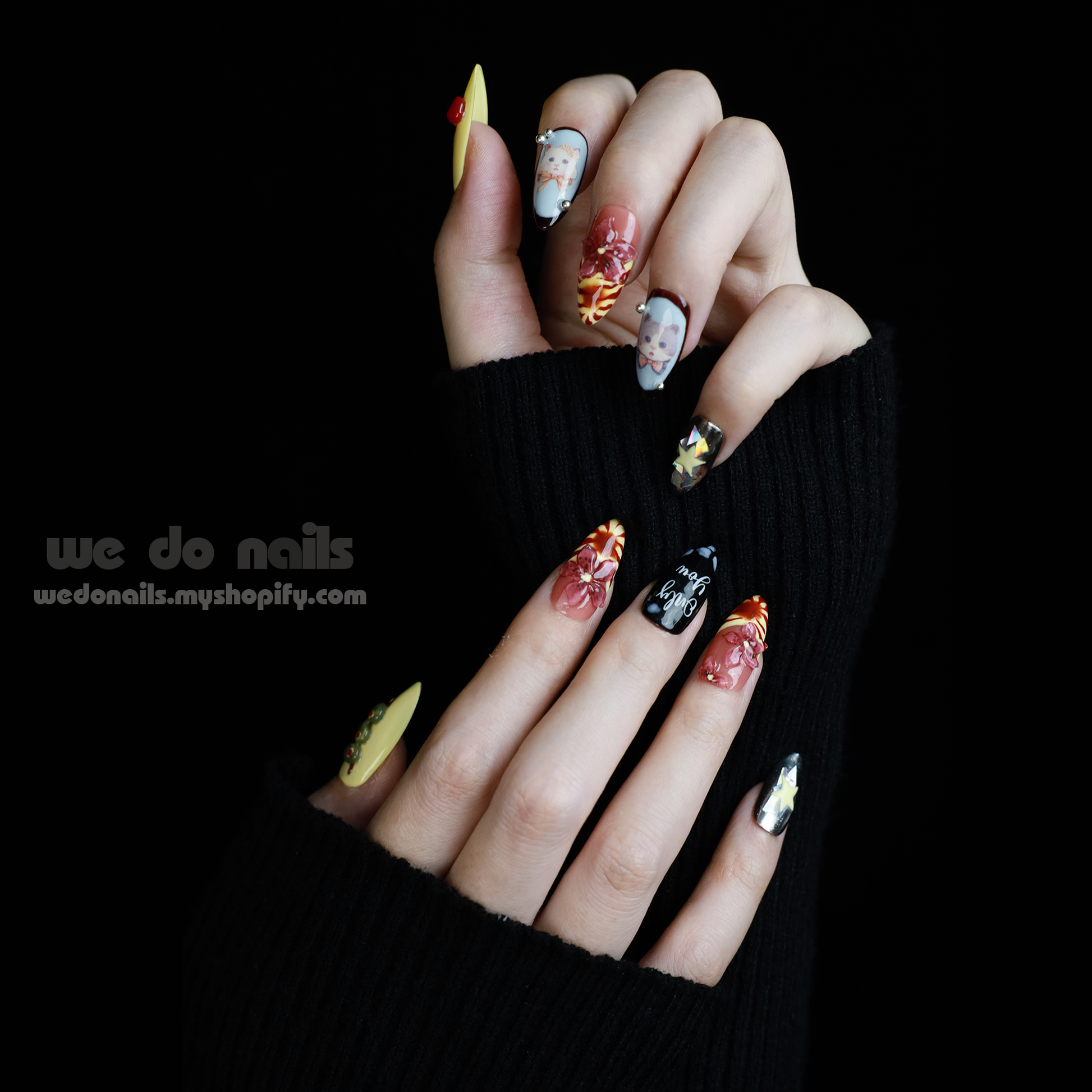 A hand adorned with We Do Nails Extravaganza Press-On Nails, showcasing unique patterns and colors, holds a small white handbag. The dazzling metallics gleam against the black background, highlighting the bold nail art and bag.