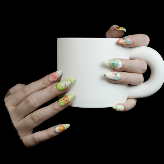 Against a dark backdrop, long-nailed hands cradle a white mug, with nails showcasing Whimsical Cottage Daydream Press-On Nails by We Do Nails. These custom designs feature intricate flowers and vibrant patterns that blend vintage aesthetics with modern flair.