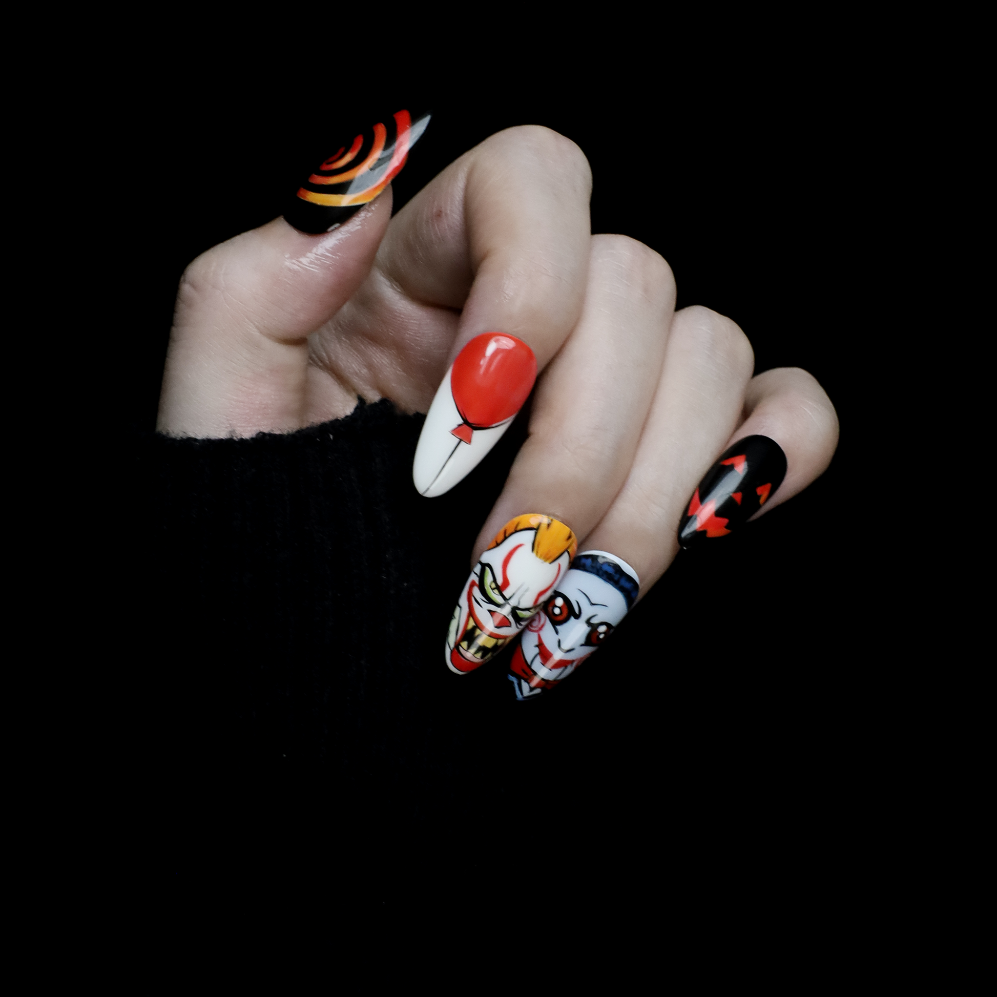 A close-up of two hands shows off the eerie Spooky Nightmares Halloween Press-On Nails by We Do Nails, featuring hand-painted designs like clowns, a pumpkin, and abstract art on a black background while holding a large white mug.