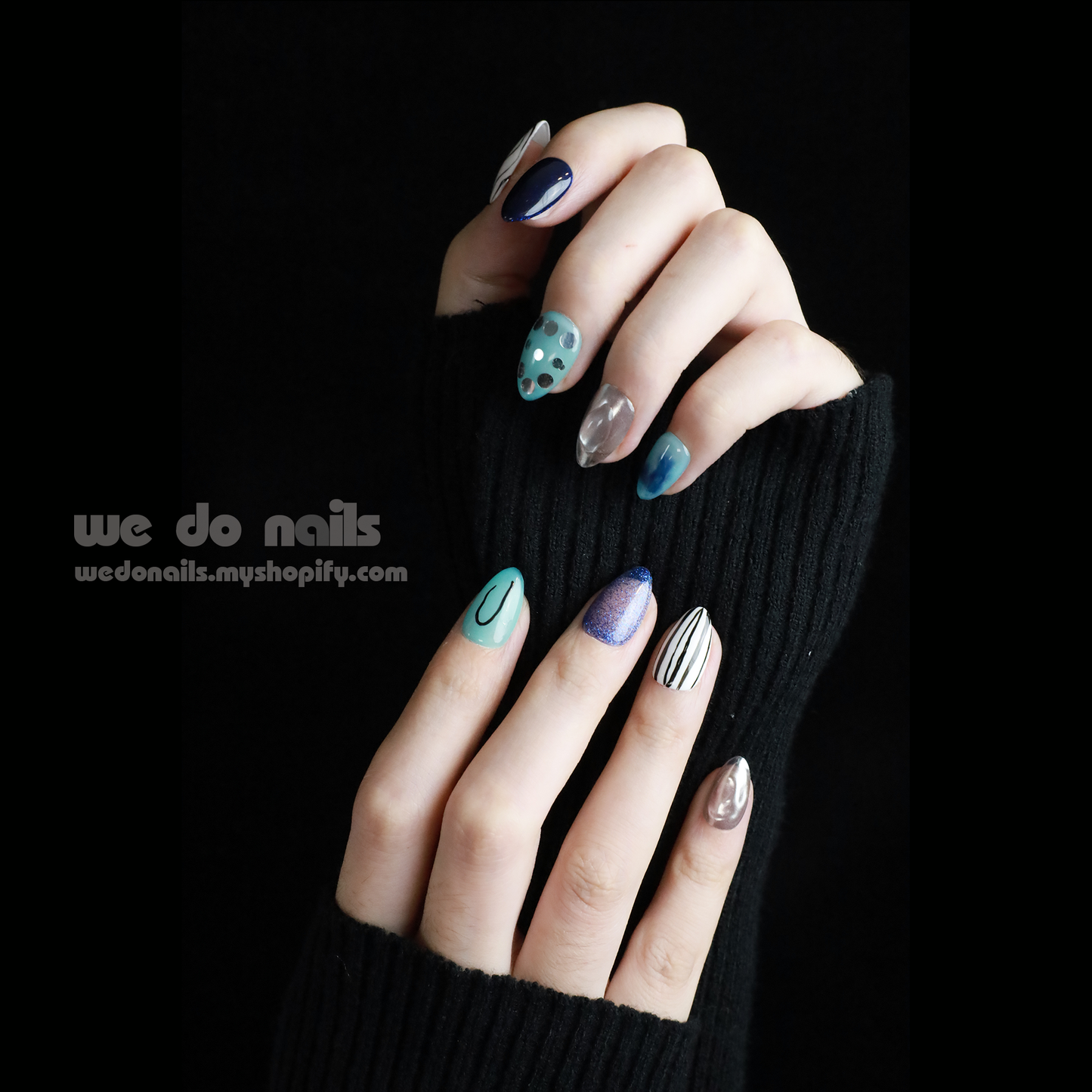 A person in a black sweater displays manicured fingernails with enchanting designs like polka dots, stripes, and abstract patterns. The metallic finishes shine in blue ombre and green hues, featuring Midnight Mystique Press-On Nails by We Do Nails. The text reads we do nails next to a website URL.
