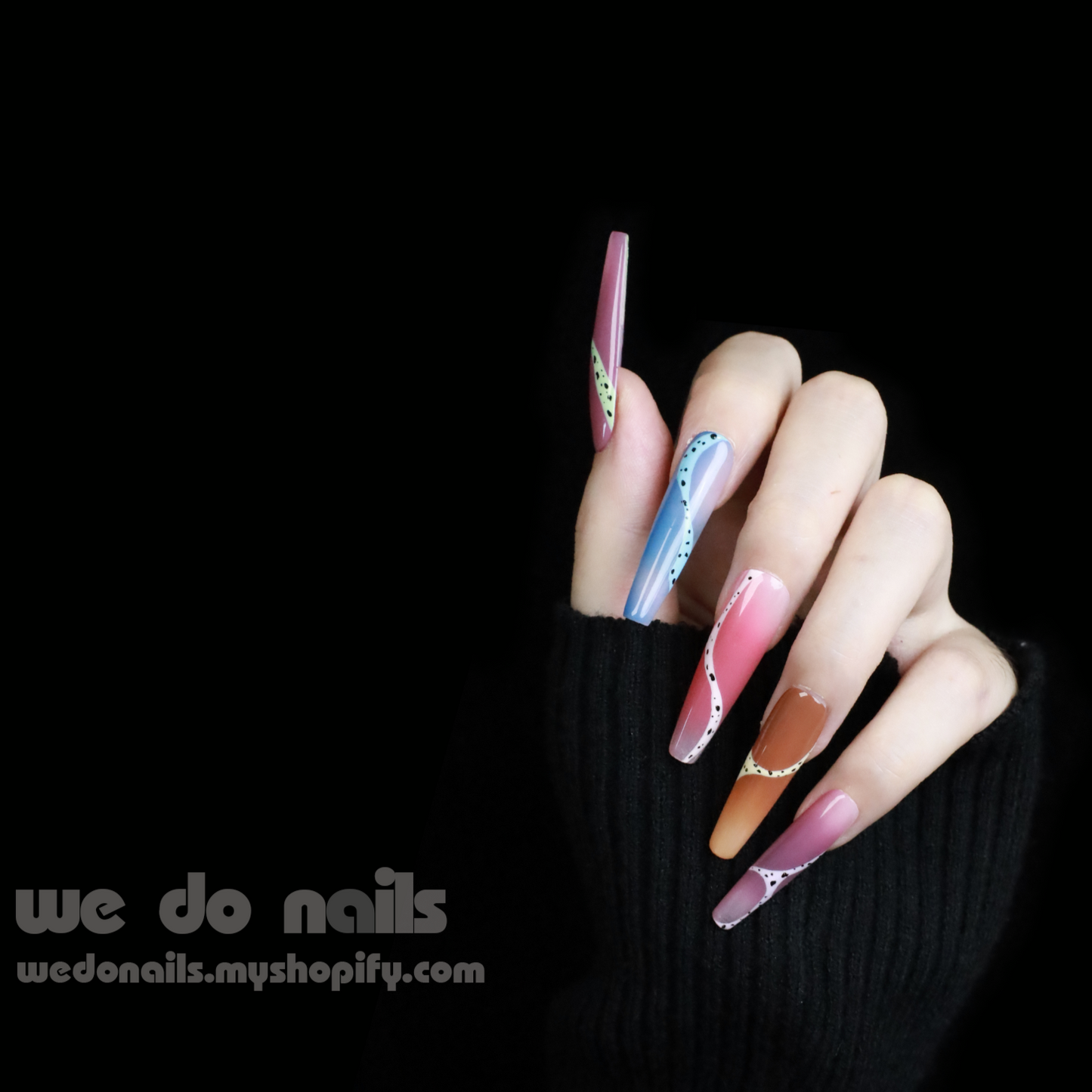A hand adorned with Milky Rainbow Press-On Nails exhibits a smooth gradient and dotted 3D designs against a black background. The text We Do Nails appears alongside the website link, emphasizing the brands artistry.