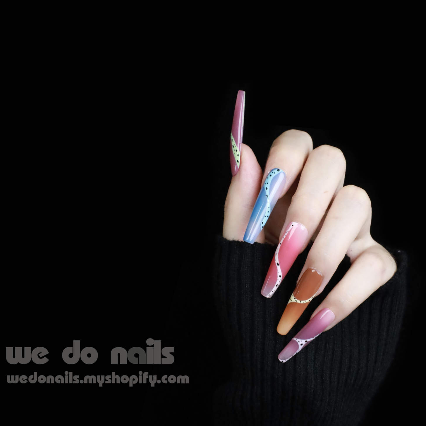 A hand adorned with Milky Rainbow Press-On Nails exhibits a smooth gradient and dotted 3D designs against a black background. The text We Do Nails appears alongside the website link, emphasizing the brands artistry.