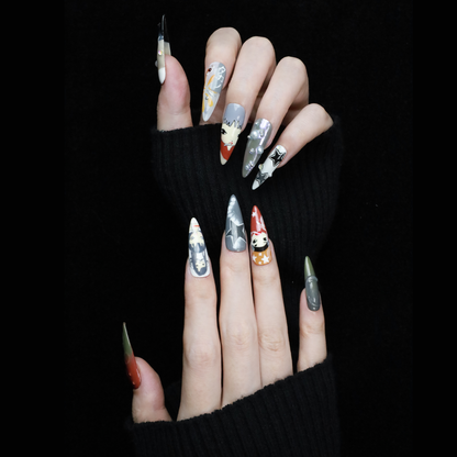 A hand with long, pointed Japanese-Inspired Artistic Press-On Nails by We Do Nails showcases camo patterns in green, red, and gray. Combining kawaii aesthetic and artistic motifs that suggest anime nail art, the hand is partially covered by a black sleeve.