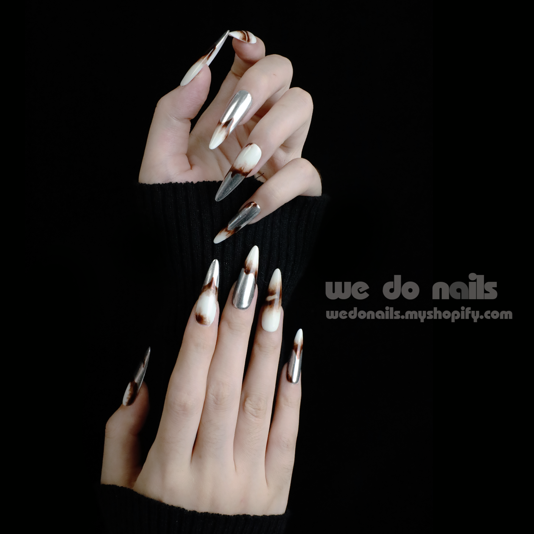 Close-up of two hands with long, pointed Sizzling Marble Press-On Nails by We Do Nails, showcasing a trendy black, brown, and white marble design. The person wears a partially covering black sleeve against a black background. Text reads we do stylish nails wedonails.myshopify.com.